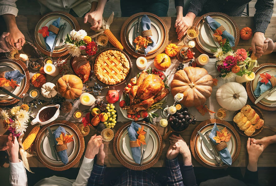 Group of friends or family members giving thanks to God at festive turkey dinner table together. Thanksgiving celebration traditional dinner concept.